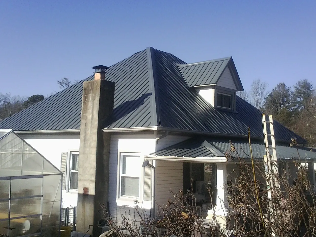 Dark blue standing seam metal roof on a white farmhouse with dormer — Slate & Tile Roof Repair by Roofing Brothers in Buckner