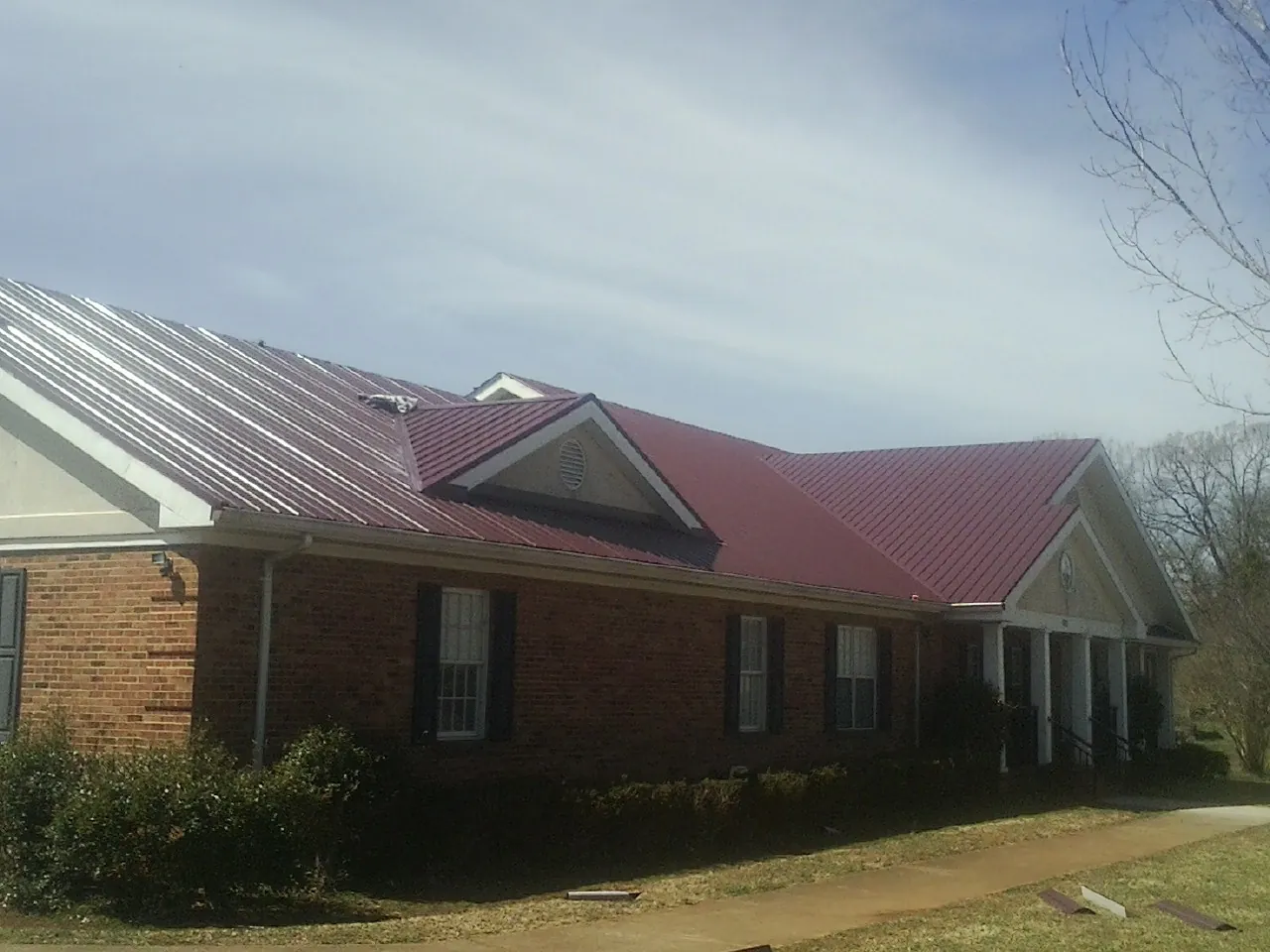 Red metal roof with gabled entries on a long brick building, from a Hail Damage Roof Repair job in Buckner