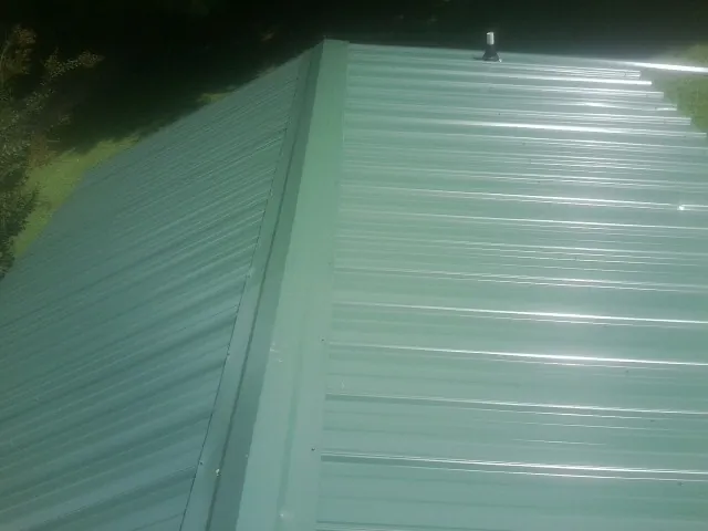 New green metal panels meeting at the ridge of a roof — Flat Roof Repair work by our crew in Buckner
