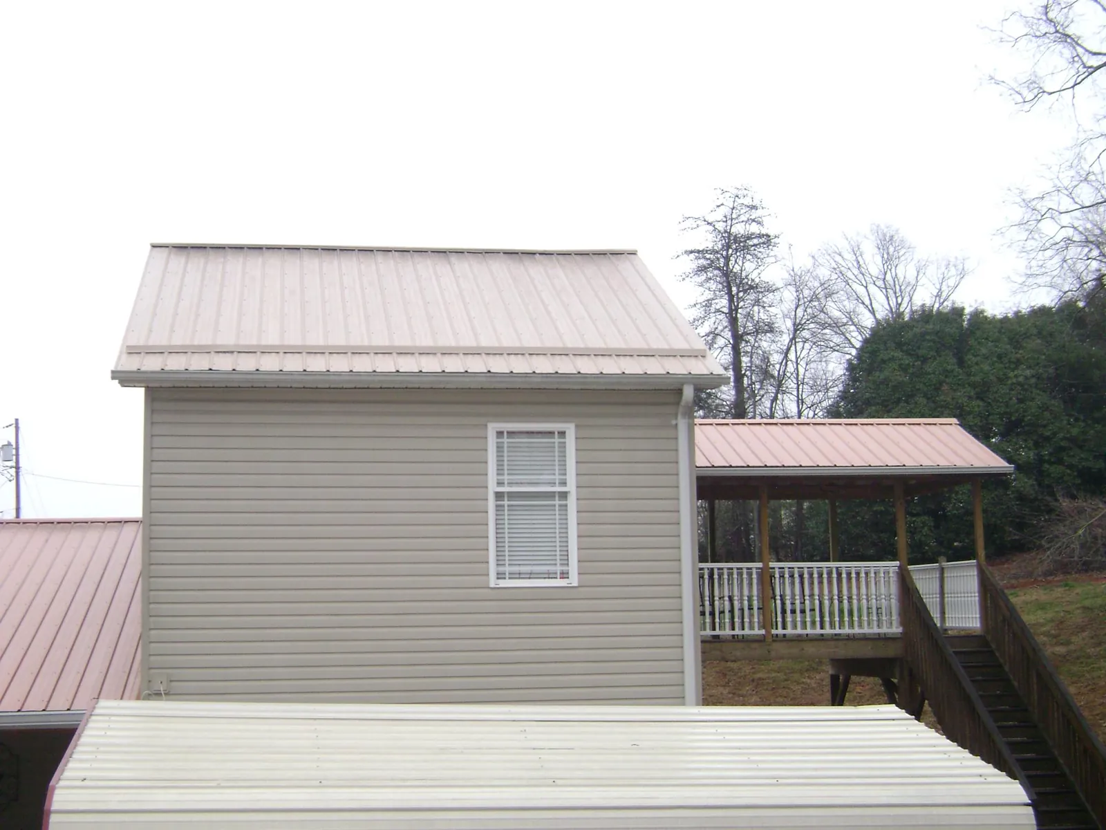 Tan metal roofs on a two story addition and attached porch, from a Roof Replacement job in Buckner